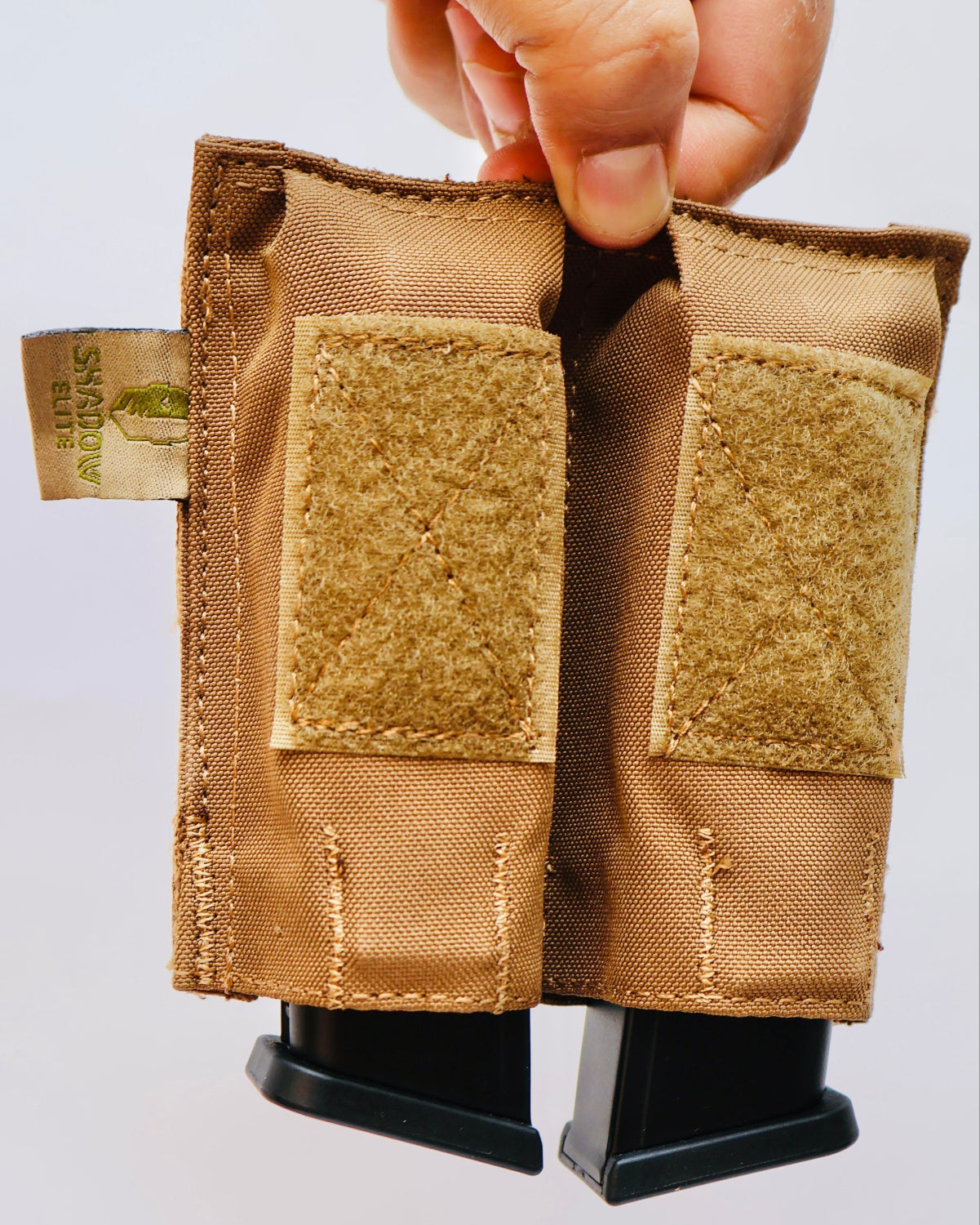 SHE-23030  Double Pistol GRIPTAC Tan tactical magazine pouch held by a hand on a light gray background