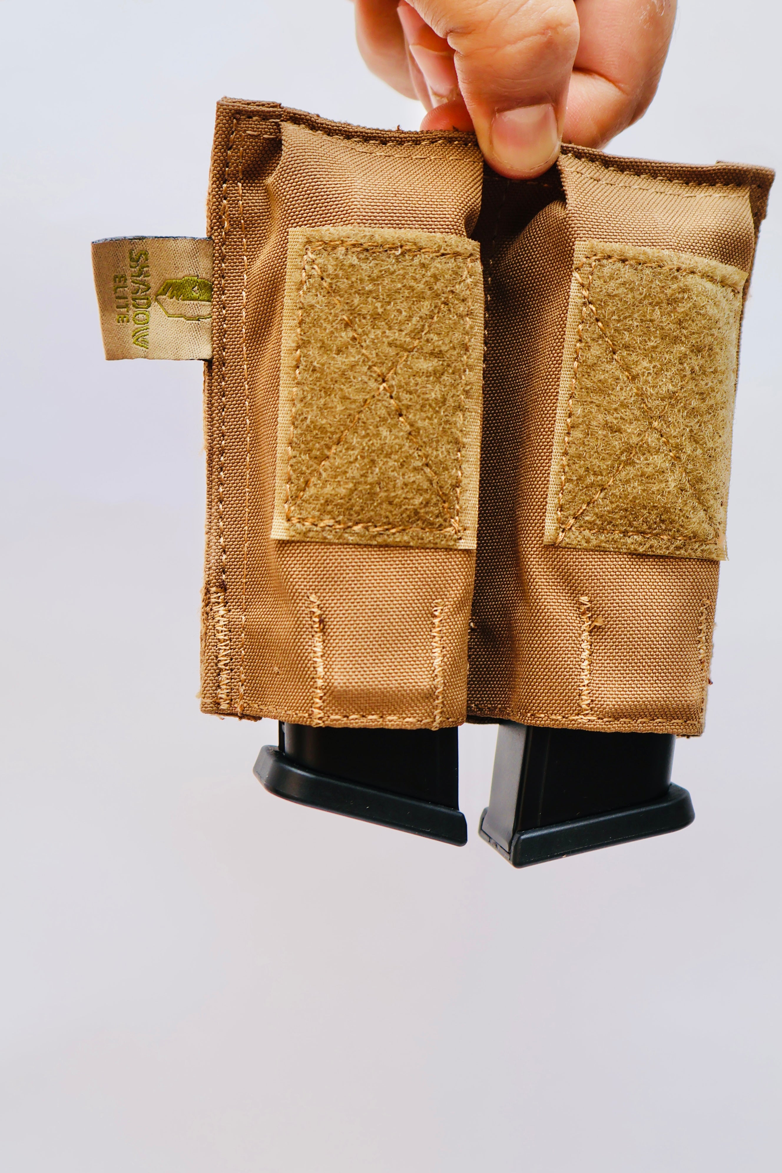 SHE-23030  Double Pistol GRIPTAC Tan tactical magazine pouch held by a hand on a light gray background
