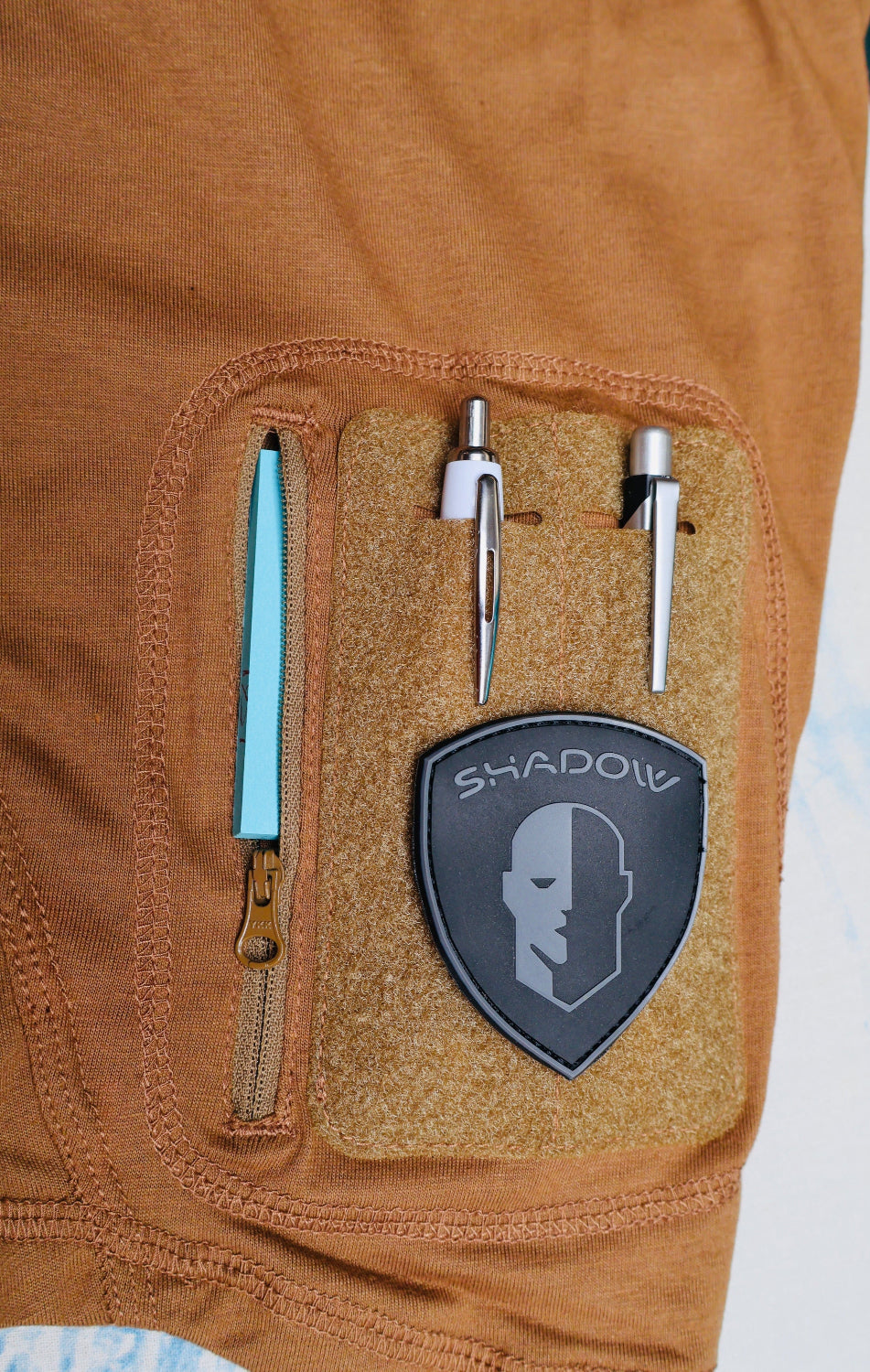 Close-up of a brown jacket pocket with tools and a 'Shadow' brand logo.