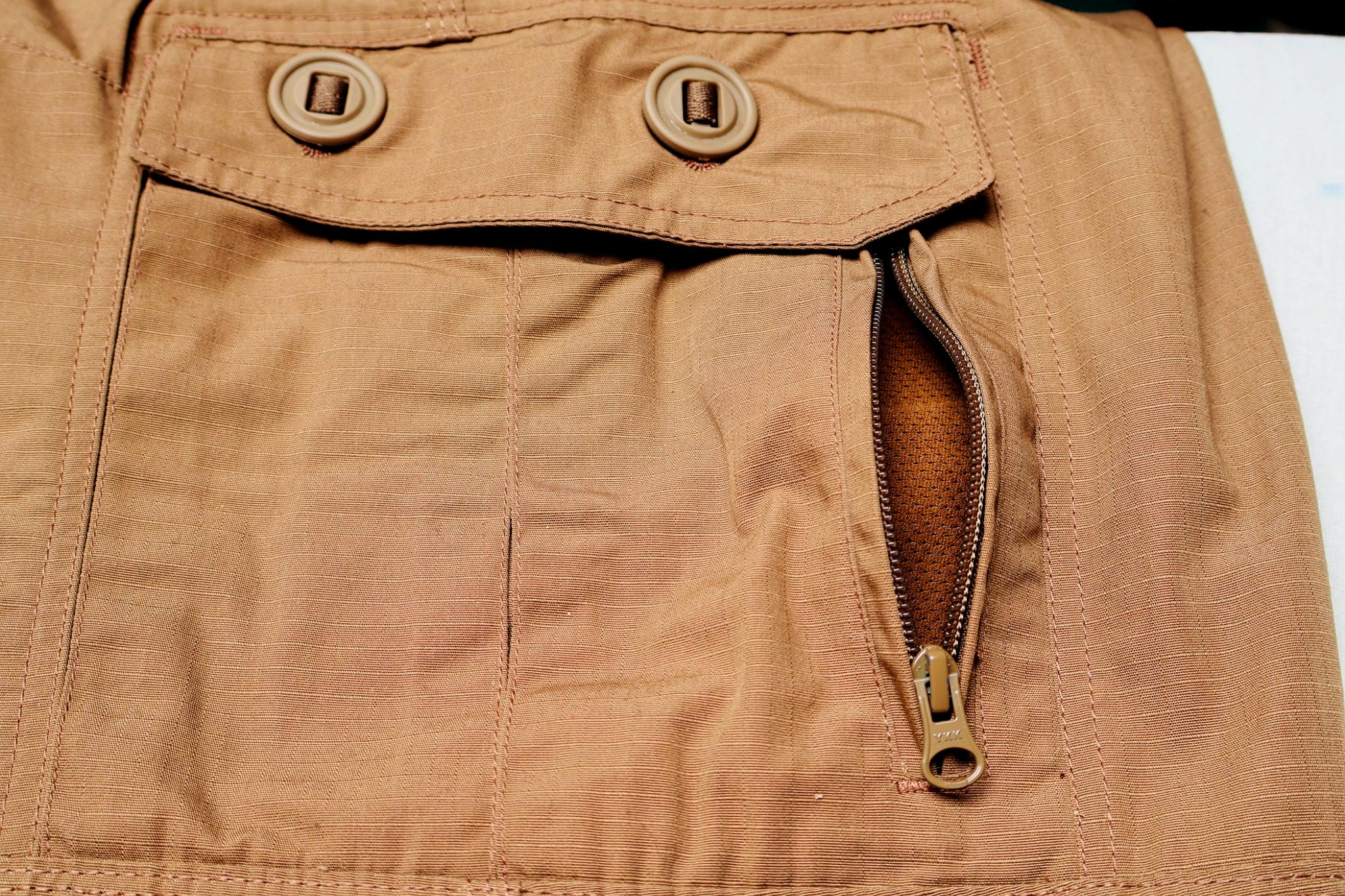 Close-up of a brown pants pocket with a zipper and buttons.